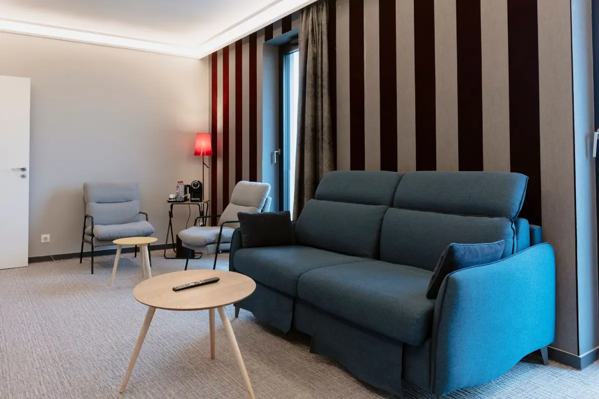 Coin salon moderne dans une chambre de l’Hôtel Dali Val d’Europe avec canapé bleu et fauteuils